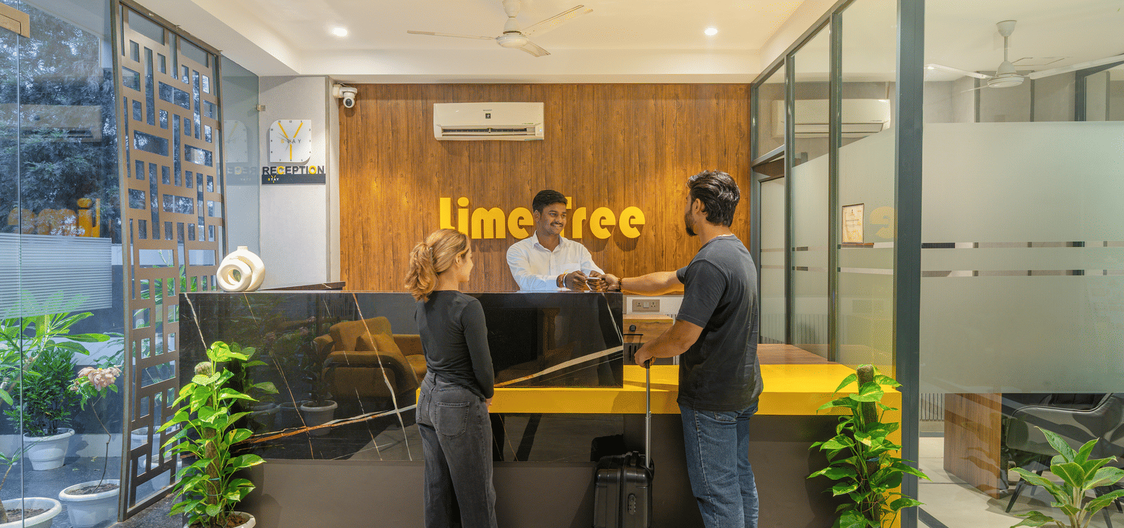 Welcoming reception area with modern interiors where two guests are speaking to the receptionist at Lime Tree Hotel & Stays Greater Noida Nearby India Expo Centre & Mart.