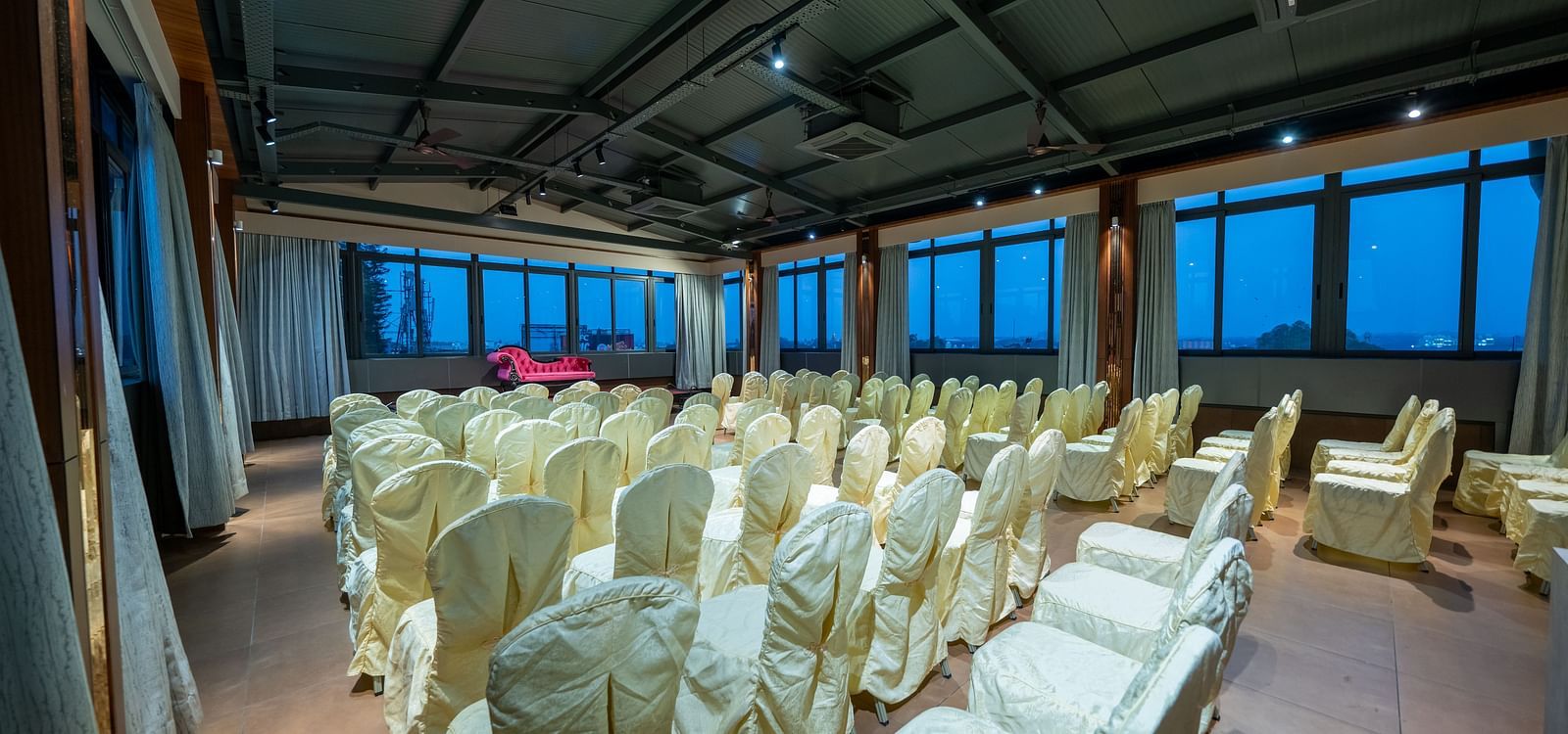 Hari Govinda's Express, Vijayanagar, features a banquet area with a central aisle, neatly arranged chairs, and a stage with a cushioned sofa.