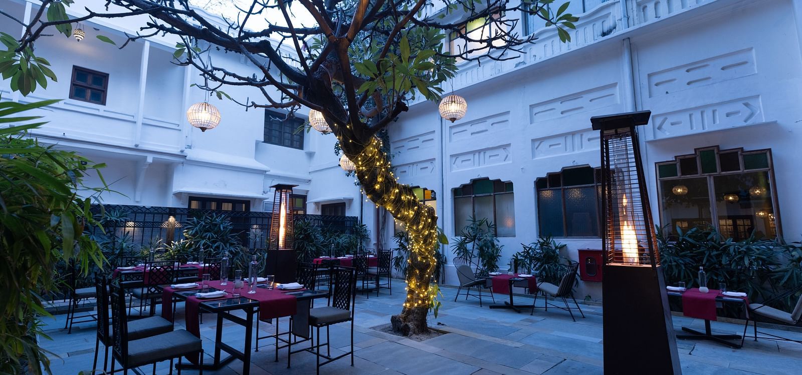 Outdoor patio area of Saraca Hotel, Lucknow with a tree in the middle during blue hour