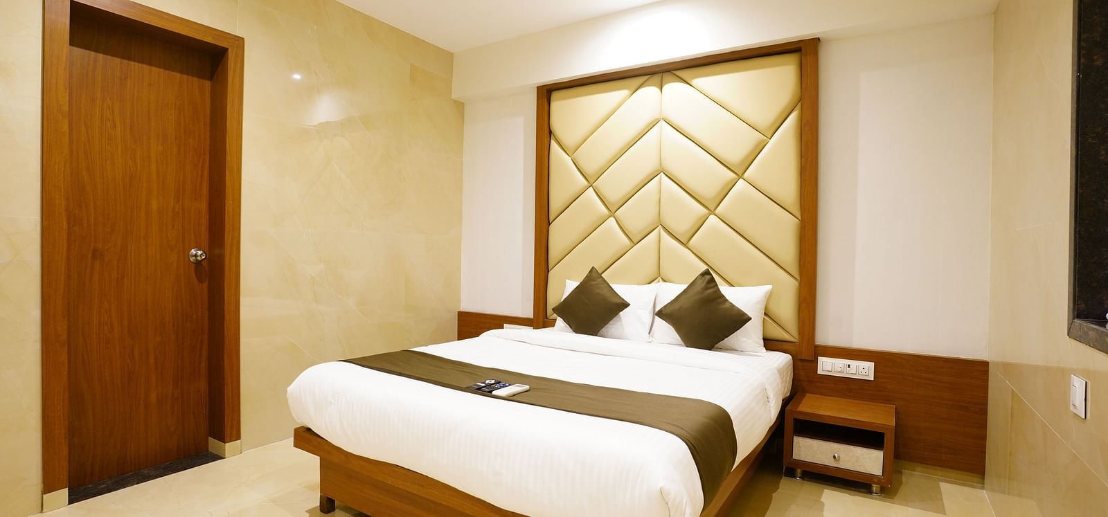 Hotel room with a double bed, patterned headboard, and closed door - Shyanu Lords Eco Inn Airoli