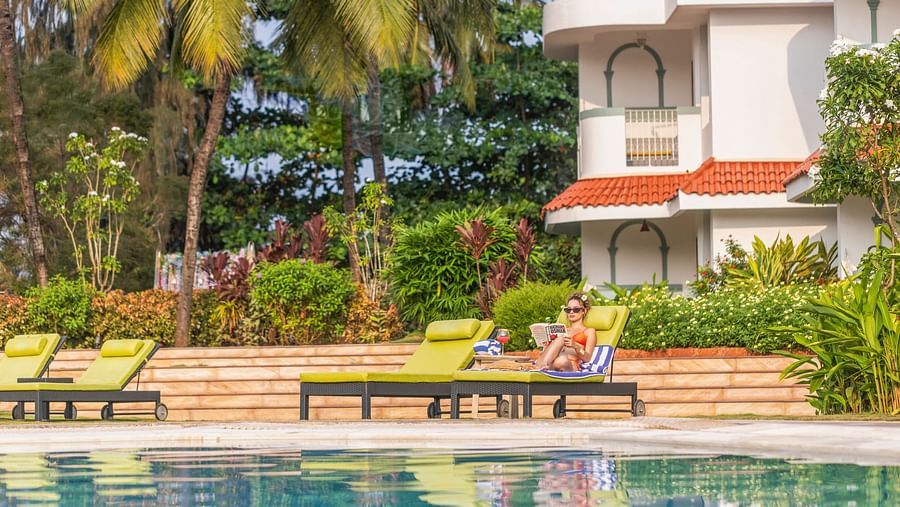 Guests relaxing on sun loungers beside a pool amidst tropical greenery.