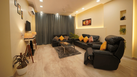 Living room of Lime Tree Hotels & Service Apartment Private Limited featuring a black leather sofa, framed wall art, and a coffee table.