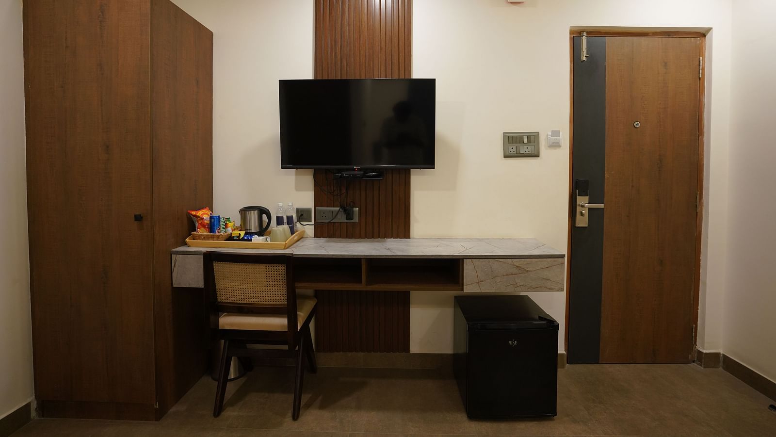 A room with a work desk, a wall-mounted TV, a hospitality tray with snacks, and a modern, minimalistic design at Hotel Kyzen Smartstays – Smart, Reliable, Kyzen