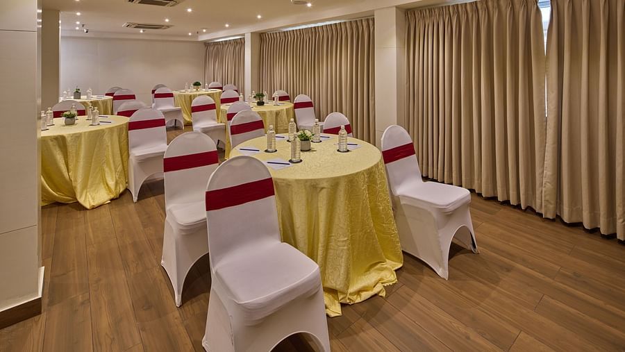 A reception hall in Bangalore with round tables and chairs covered in white cloth turned towards the speaker - Grand Continent, Brookefield