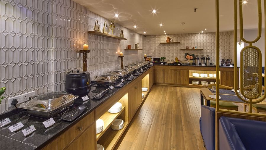 A buffet area with a shelf of delicious fruits, bread, and cake, set under wooden shelves and lit by warm yellow lights - Grand Continent, Brookefield