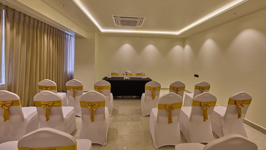 A well-lit banquet hall with white-covered chairs facing a table covered with navy blue cloth