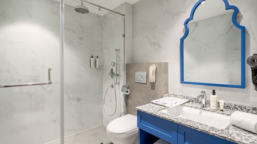 A picture of a bathroom with a separate shower cubicle, a large wall mirror, a sink, and a wall-mounted bathroom phone - MJ Sarovar Portico, Haridwar