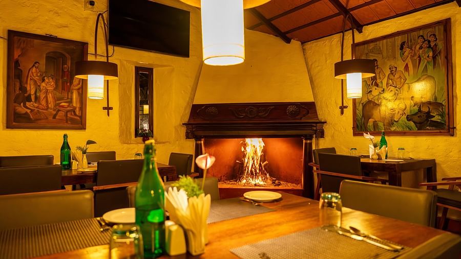 Warmly lit dining area with wooden furniture and decorative wall art. | Mango Hill, Yercaud