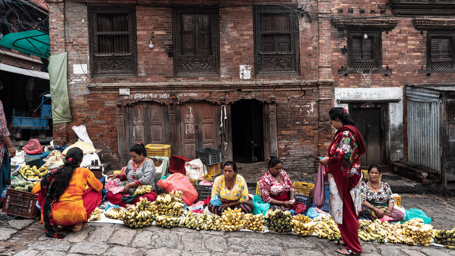 Local women selling fresh vegetables on the pavement in front of an ancient brick building in historic Bhaktapur, Nepal.