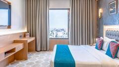 Deluxe Room at Pride Elite Dwarka featuring  a double size bed, a cabinet table, a flat TV screen, and a window with curtains.