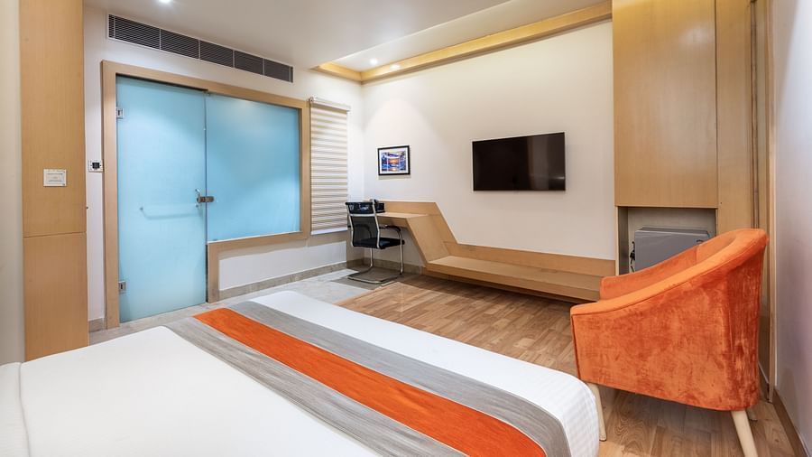 An image of the deluxe room at DLS Hotel Arihant, Haridwar with a bed, a chair, and a flat screen TV