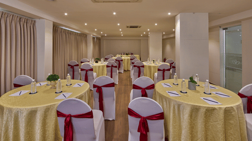 An image of an air-conditioned banquet hall in Bangalore with warm ceiling lights, round tables, chairs and black-out curtains - Grand Continent, Brookefield