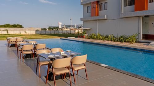 dining tables and chairs across the pool with the hotel in the back of Pride Elite Becharaji