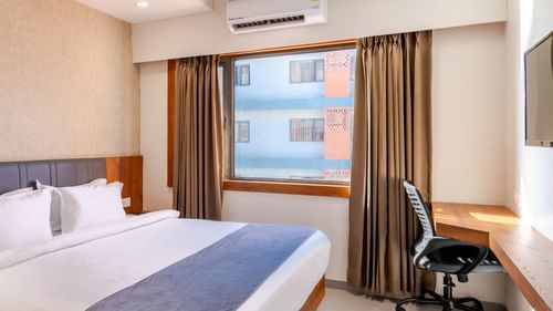 Premium Room at Pride Elite Wellness Resort Becharaji, Gujarat featuring a plush bed next to a window and a work desk in a corner with a chair facing the wall