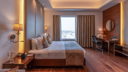 Wooden floor suite featuring a plush bed in ambient lighting with lamps on both sides of the bed and daylight making its way through the large window