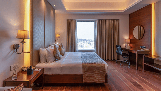 Wooden floor suite featuring a plush bed in ambient lighting with lamps on both sides of the bed and daylight making its way through the large window