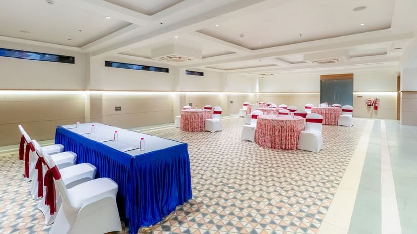 Banquet Hall at Pride Comfort Dwarka featuring conference table with chairs, and other sets of tables and chairs decorated with ribbons and fabrics for guests.