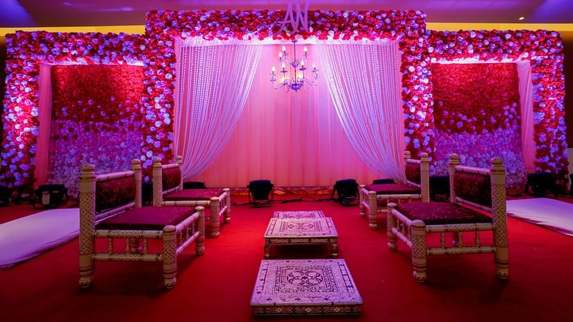 A celebratory stage with flower decorations, two red chairs and two tools within modern lighting giving a red  and lilac hue of the place