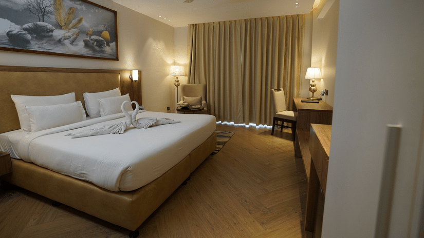 A warm-lit room featuring a king-size bed with a painting above the headboard and a work desk in the corner