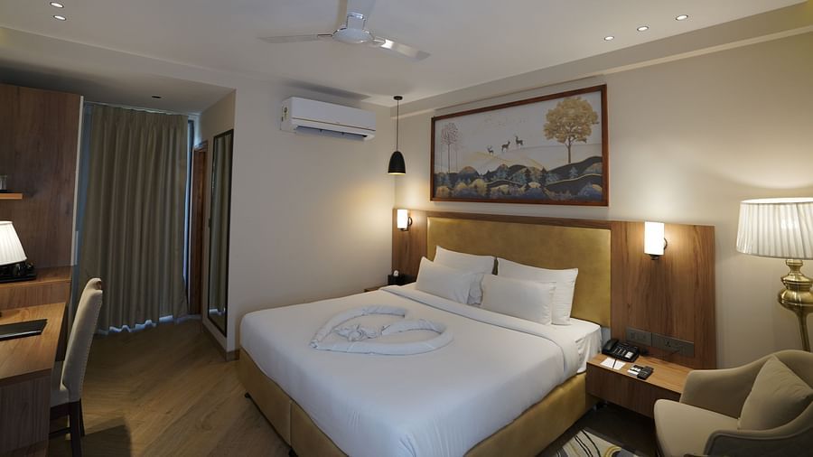 A warm-lit room featuring a king-size bed with a painting above the headboard and an AC mounted next to it