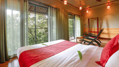 A bed placed in a room with tall glass windows and ambient lighting | Vythiri Resort, Wayanad