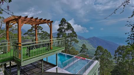 Balcony with a view of the ground-floor swimming pool, surrounded by trees and hills - Fragrant Nature Munnar