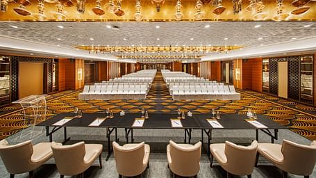 Banquet hall featuring a luxurious golden ceiling and rows of white chairs at Radisson BLU