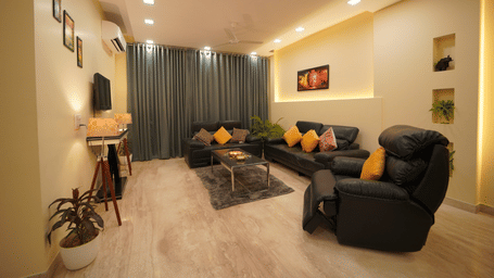 Living room of Lime Tree Hotels & Service Apartment Private Limited featuring a black leather sofa, framed wall art, and a coffee table.