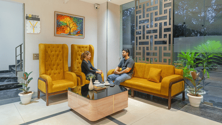 People seated on a yellow sofa in a lounge area of Lime Tree Hotels & Service Apartment Private Limited featuring wall art and potted plants.