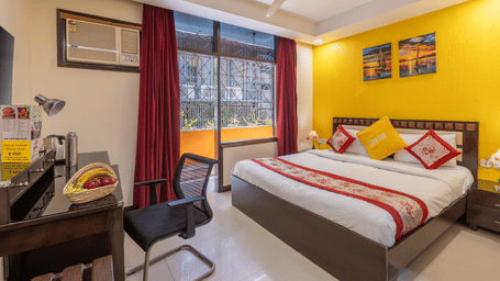 Bedroom of Lime Tree Hotels & Service Apartment Private Limited featuring a yellow accent wall, red bedding, and a ceiling fan.