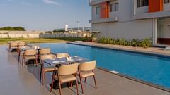 dining tables and chairs across the pool with the hotel in the back of Pride Elite Becharaji
