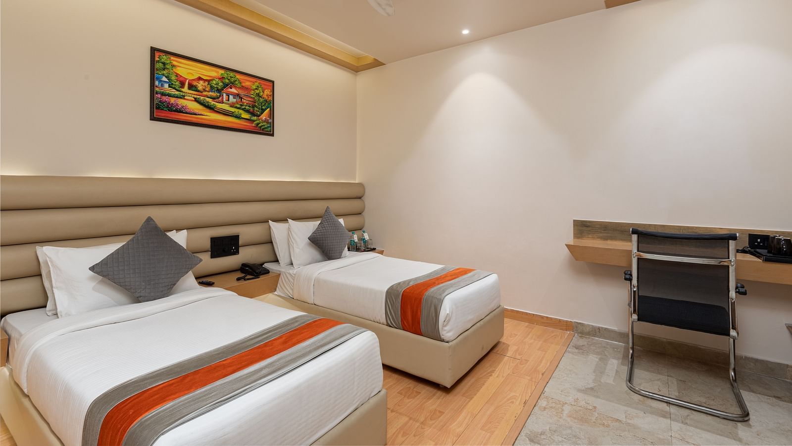 The deluxe twin room at DLS Hotel Arihant, Haridwar with two beds, a chair and a work desk