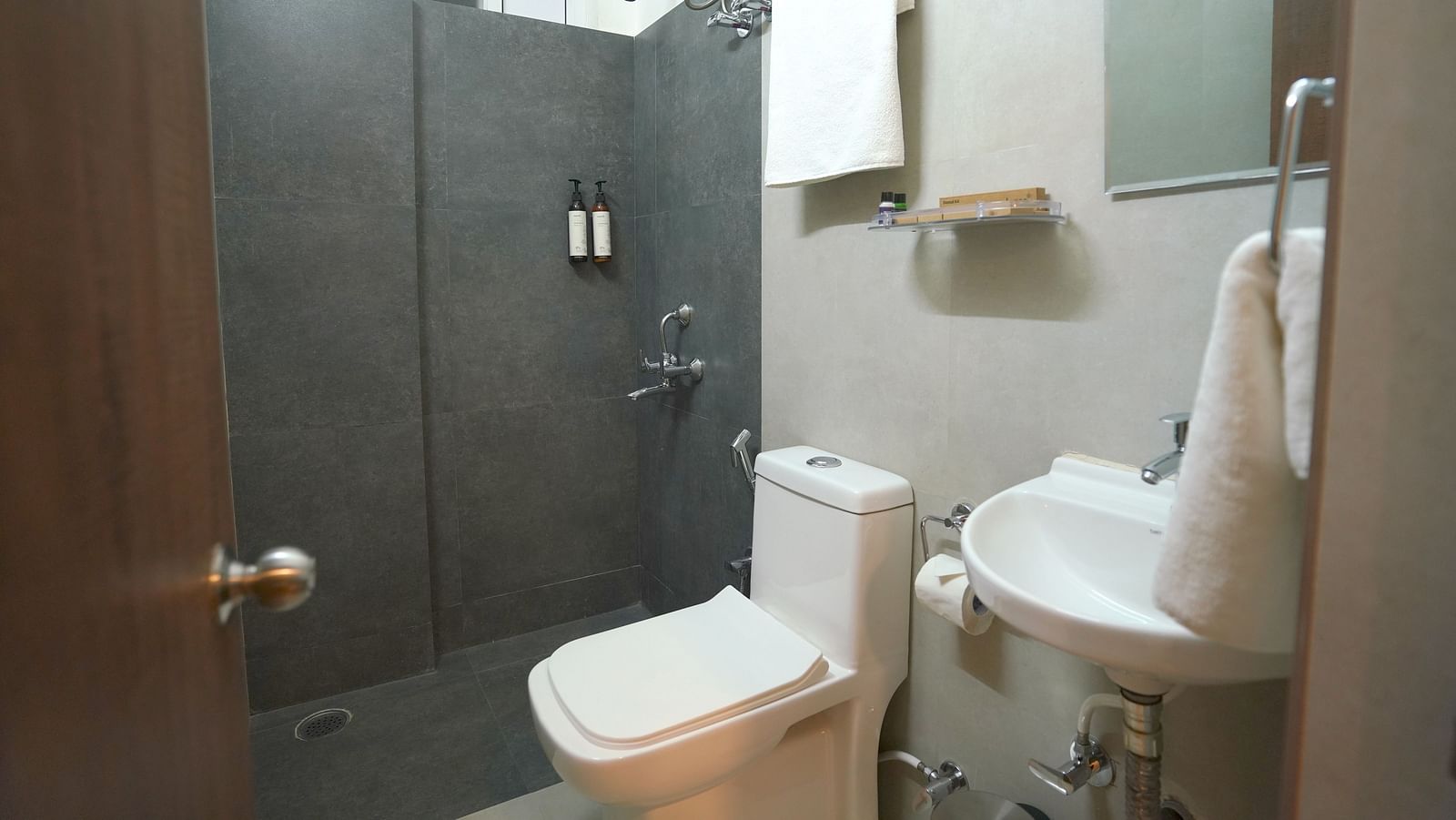 A modern bathroom at Kyzen Smart Stays in Hyderabad featuring a toilet, shower, and dark grey walls, suggesting a minimalist and functional design.
