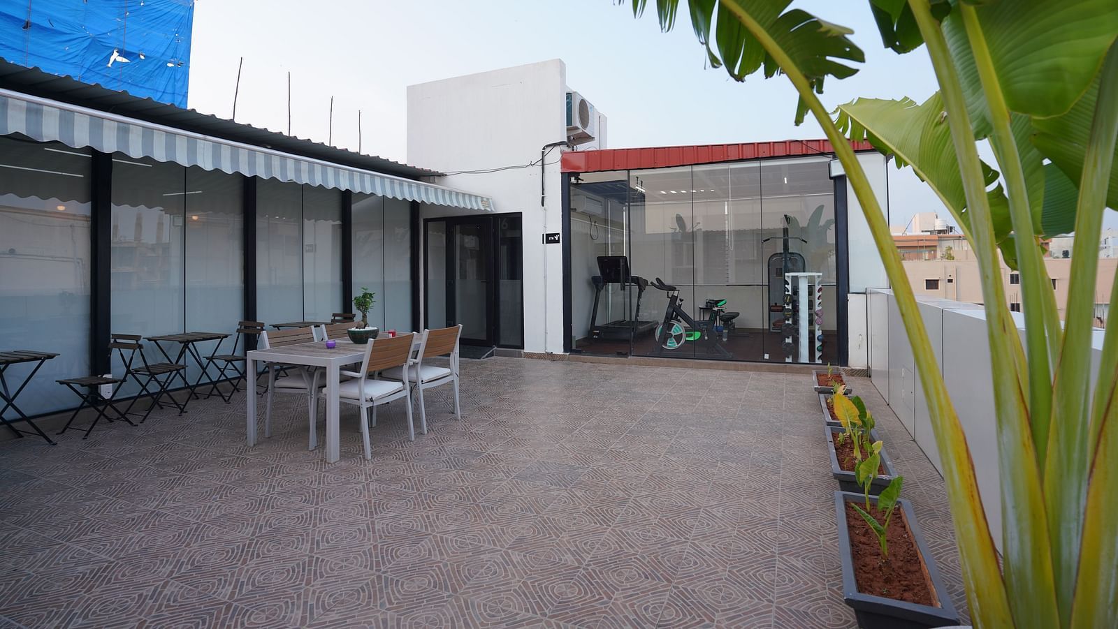 A spacious rooftop dining area with tables and chairs, surrounded by some plants at Kyzen Smart Stays.