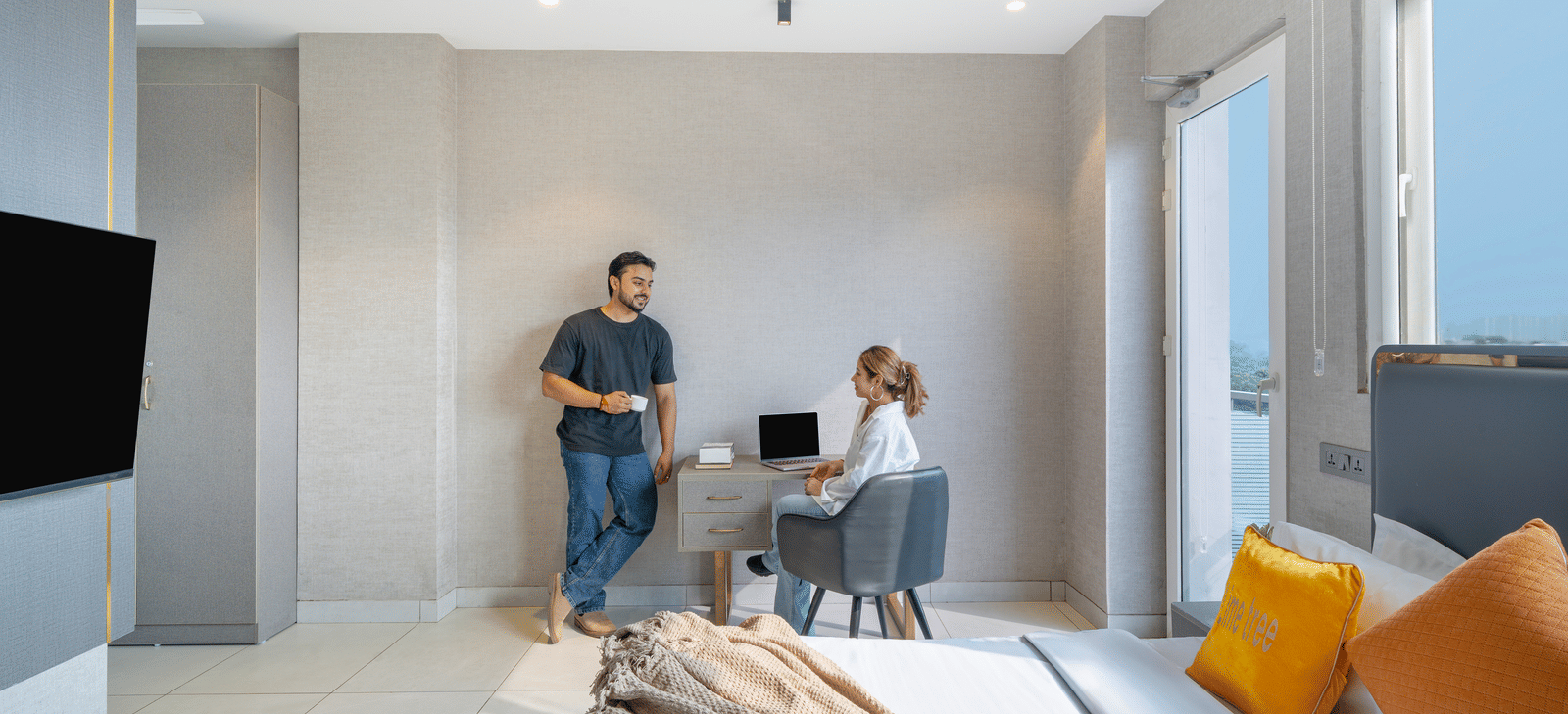 Spacious room with one person sitting at the study desk and another standing beside it at Lime Tree Hotel & Stays Greater Noida Nearby India Expo Centre & Mart.