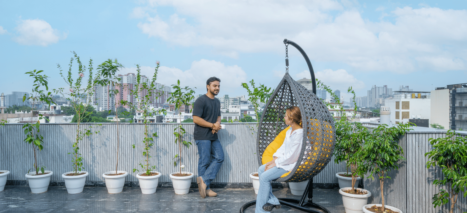 Rooftop terrace with a swing chair, one person seated and another standing beside them at Lime Tree Hotel & Stays Greater Noida Nearby India Expo Centre & Mart.