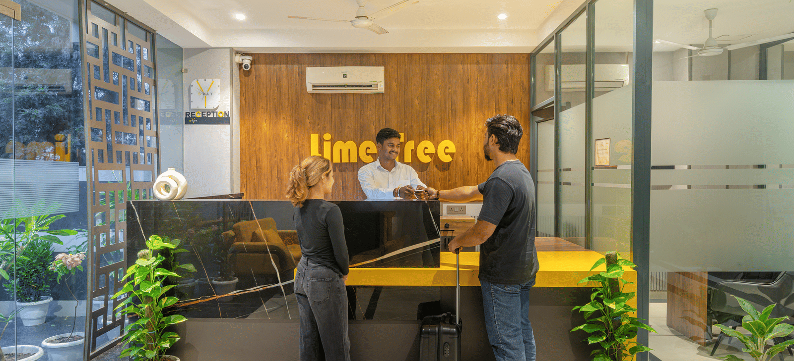Welcoming reception area with modern interiors where two guests are speaking to the receptionist at Lime Tree Hotel & Stays Greater Noida Nearby India Expo Centre & Mart.