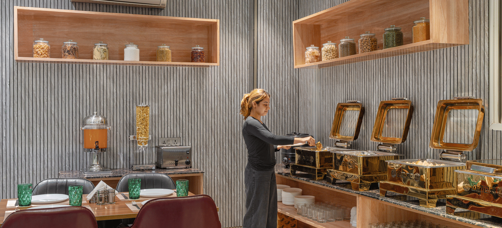 Dining area with tables and chairs, buffet arranged along the wall, and a person self-serving at Lime Tree Hotel & Stays Greater Noida Nearby India Expo Centre & Mart.