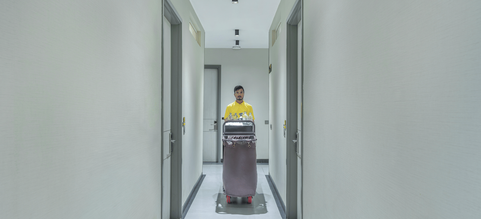 Bright corridor with clean design and polished flooring, with a staff member pushing a tray of essentials to be placed in rooms at Lime Tree Hotel & Stays Greater Noida Nearby India Expo Centre & Mart.