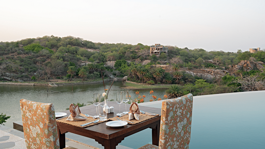A table for two set next to the swimming pool with views of the forest next to the lake - Chunda Shikar Oudi, Udaipur