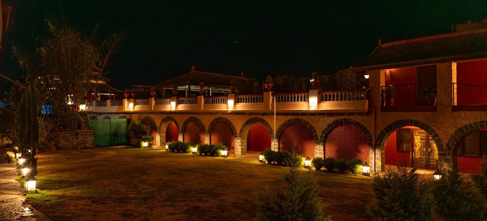 Exterior view of a well-lit building with arches at night, surrounded by a garden.  | Mango Hill, Yercaud