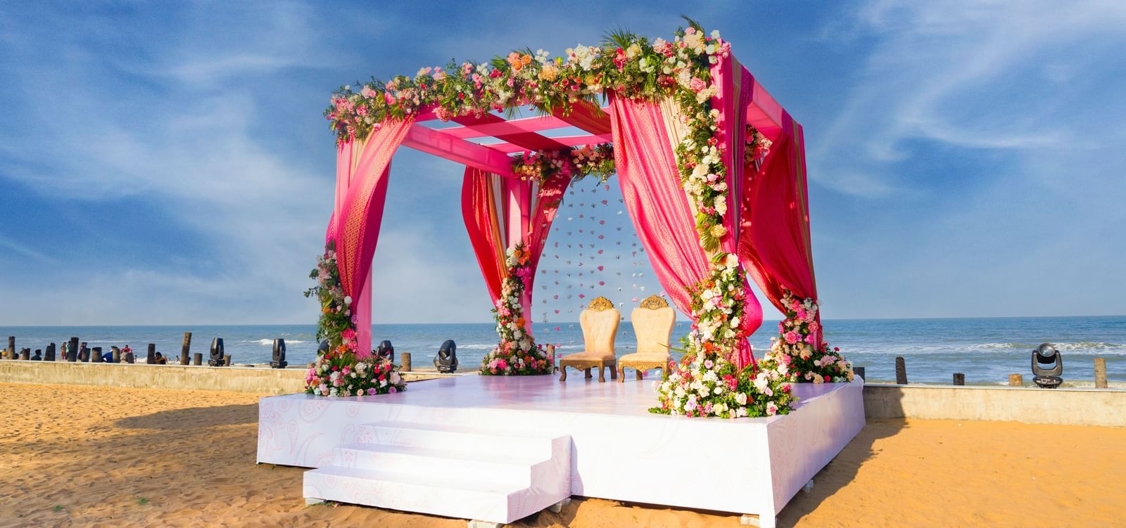 An outdoor stage decorated with pink and flowers featuring blue sky & the sea at the backdrop at Grande Bay Resort & Spa.
