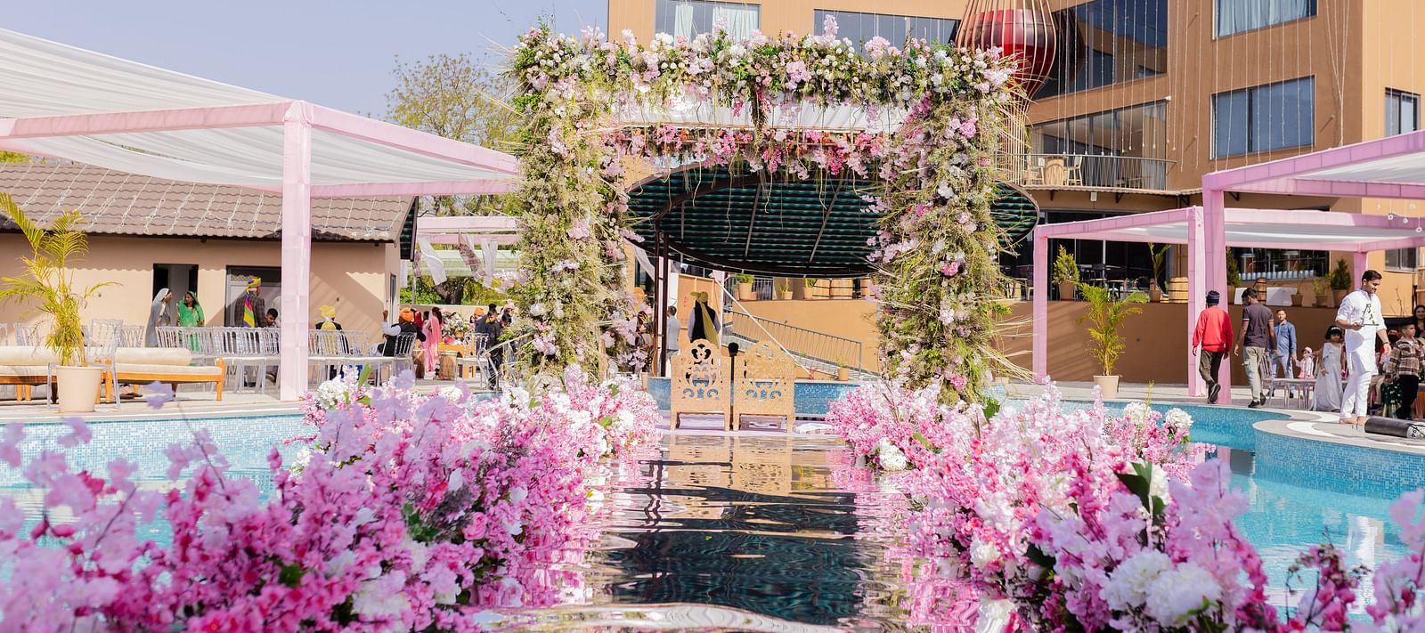 An outdoor venue showcases floral decor around a pool area and buildings | The Qualia Resort Club & Brewery, Udaipur