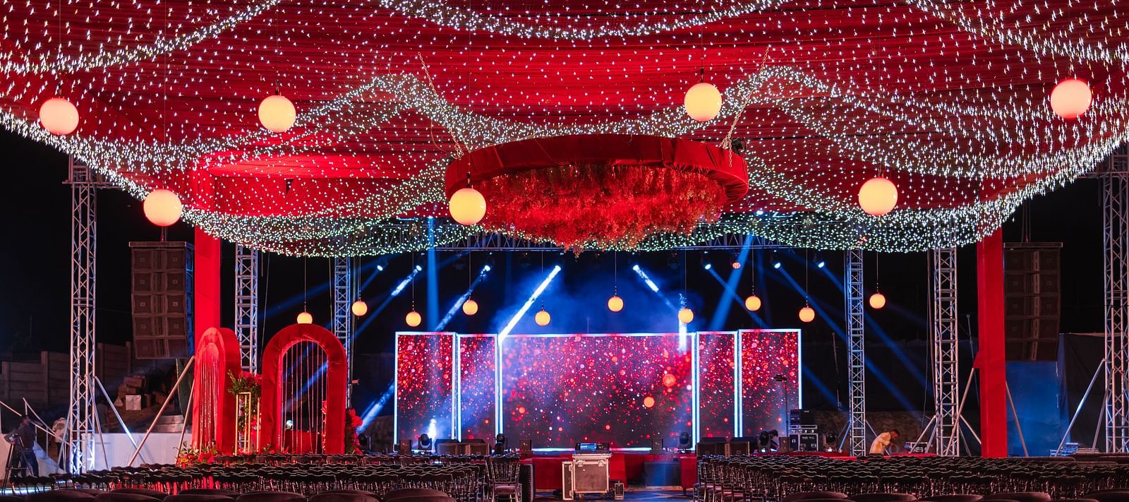 A wedding stage is decorated with red draping and lights indoors | The Qualia Resort Club & Brewery, Udaipur