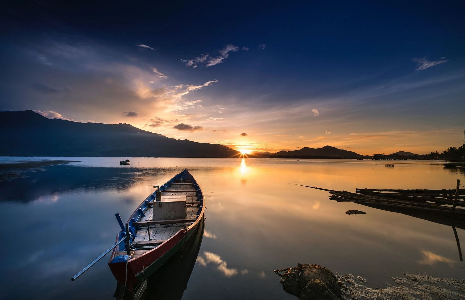 Boat on a lake at sunrise, with a dramatic sky and silhouetted shoreline.