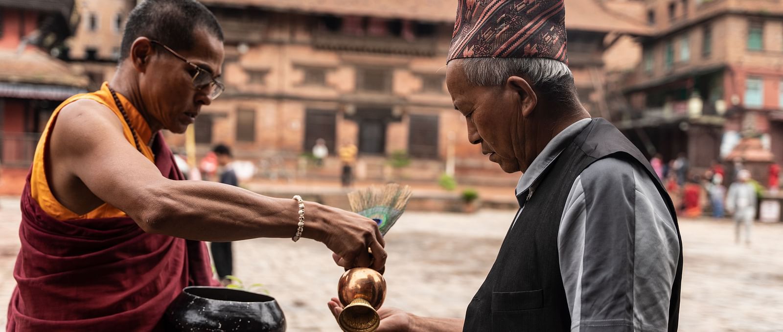 A monk pouring holy water into the palm of an old man