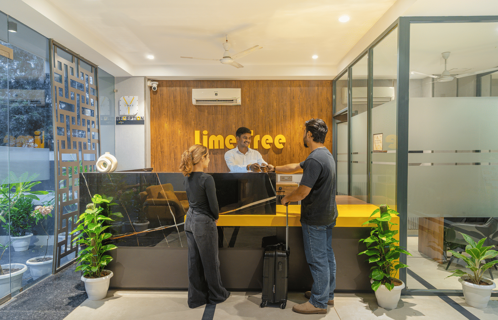 Welcoming reception area with modern interiors where two guests are speaking to the receptionist at Lime Tree Hotel & Stays Greater Noida Nearby India Expo Centre & Mart.