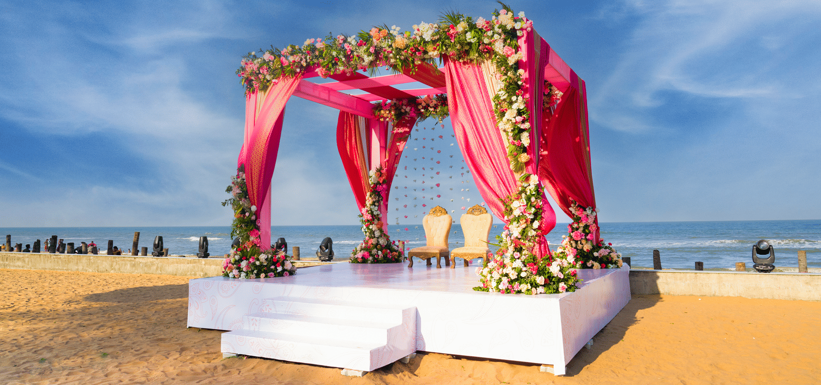 Pink floral mandap setup on the beach with draped fabric and white platform - Grande Bay Resort & Spa, Mamallapuram