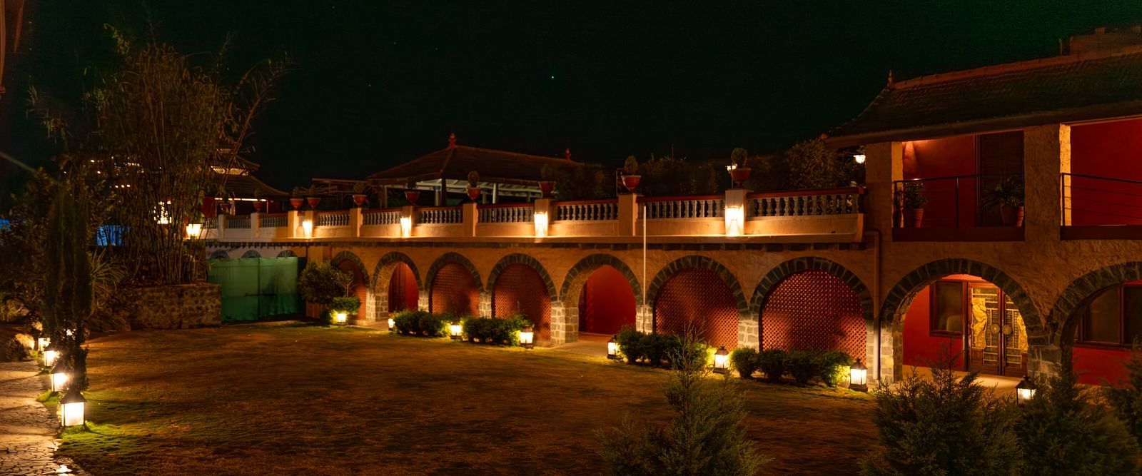Exterior view of a well-lit building with arches at night, surrounded by a garden.  | Mango Hill, Yercaud