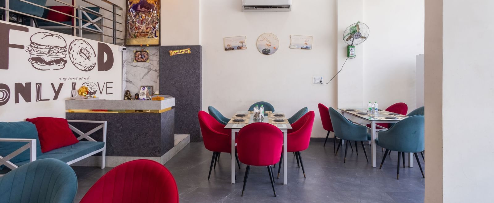 Dining area with red and blue chairs, tables, and wall art at Pravasa Stay Dewas Naka, Indore.